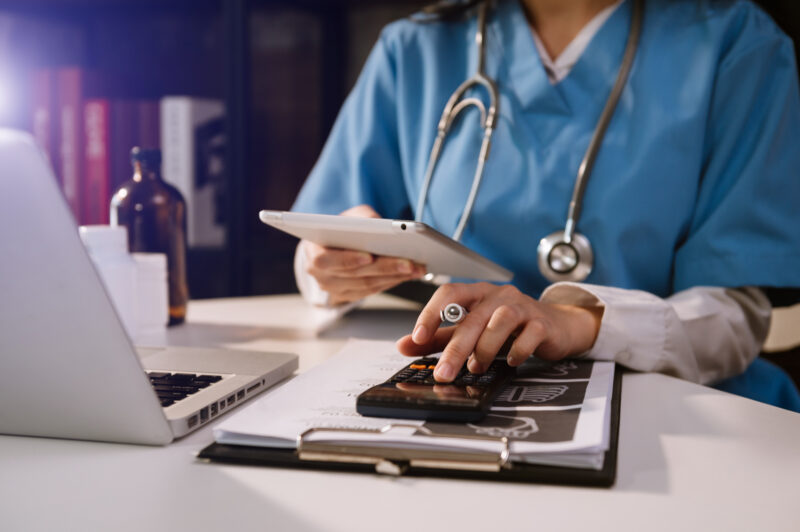 Healthcare costs and fees concept.Hand of smart doctor used a calculator and smartphone, tablet for medical costs at hospital in morning light