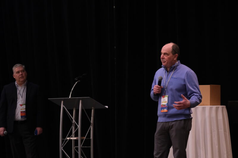 Pierre Morrisseau speaking on stage to a large audience.