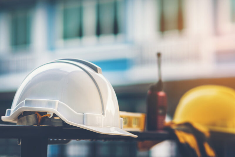 White and yellow helmet with construction water,gloves and radio that are placed on steel house fence.