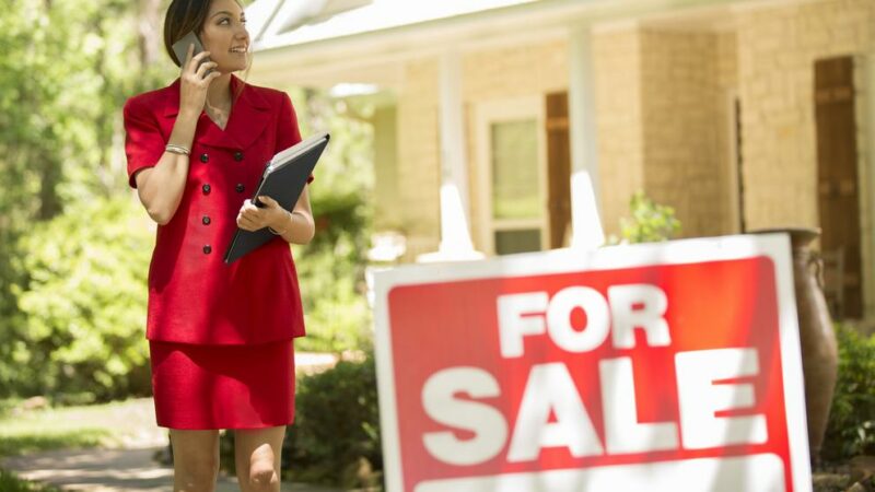 Realtor outside home for sale with real estate sign. Protect your agency with the right insurance coverage.