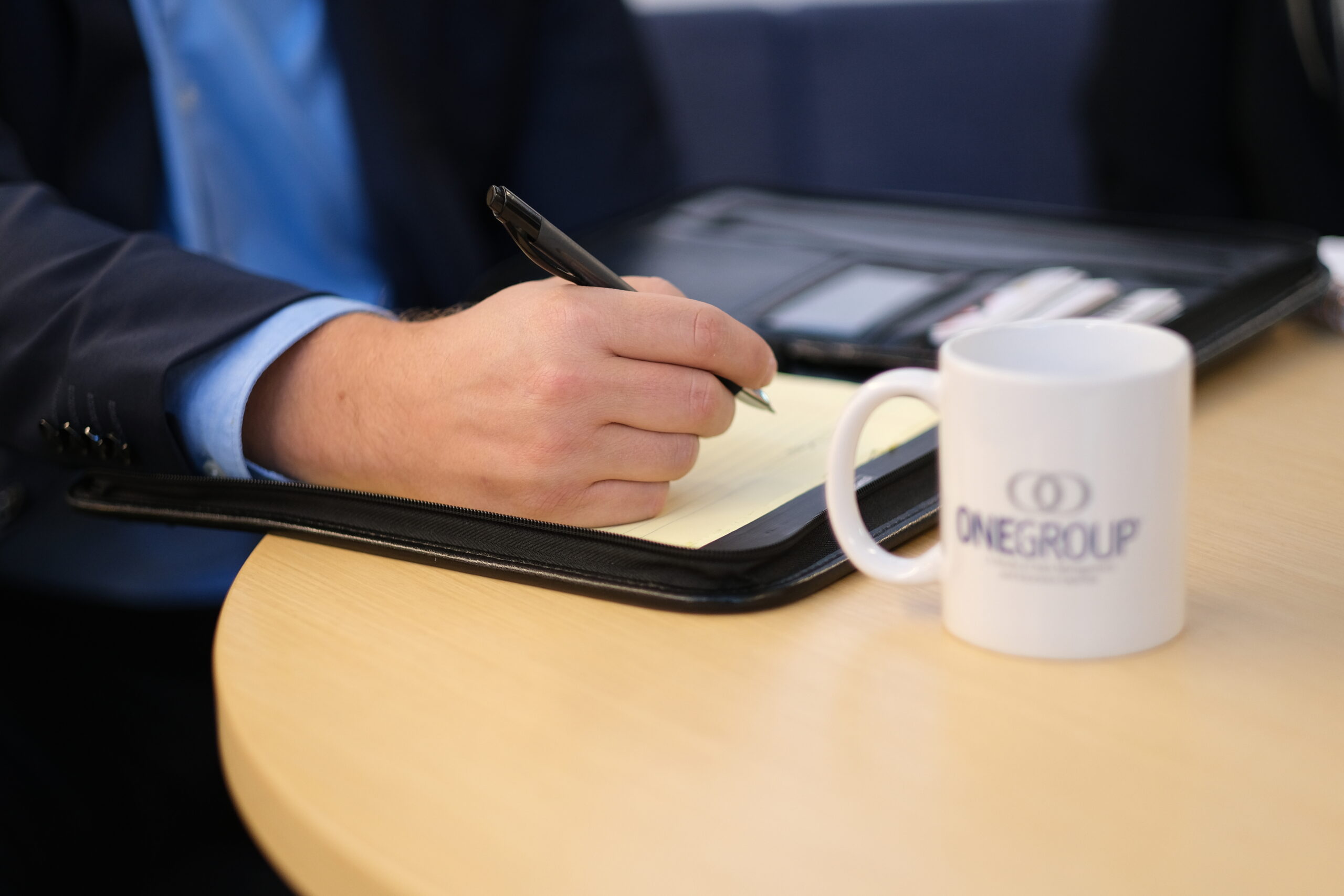 OneGroup Coffee Cup Man in Suit Taking Notes Meeting