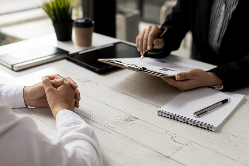 Two people sitting across a desk from each other one with a clip board