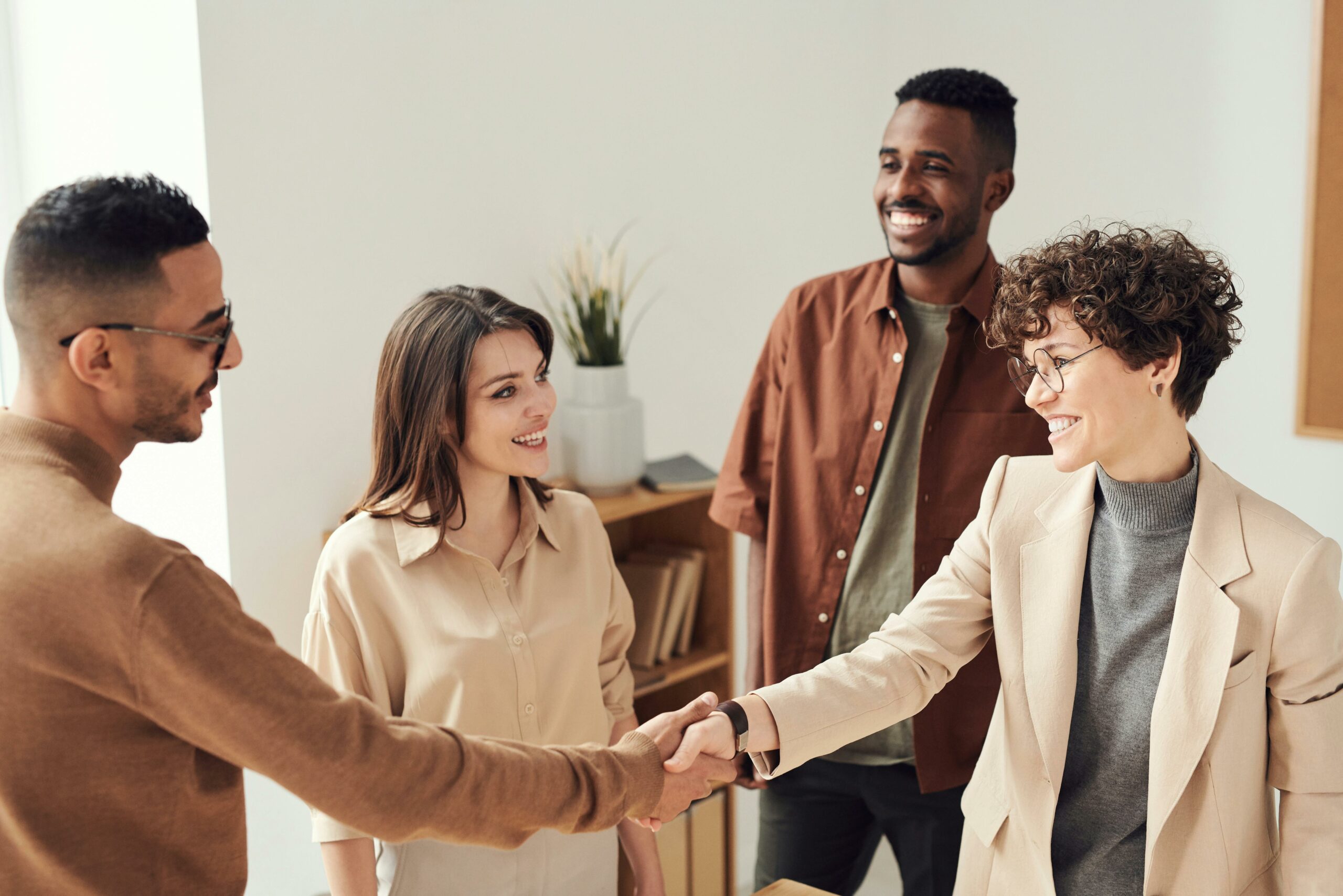 Group of coworkers standing together while two coworkers shake hands.